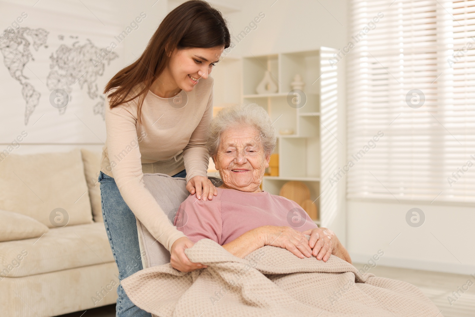 Photo of Granddaughter covering her grandmother with blanket at home. Elderly care