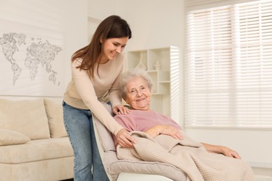 Photo of Granddaughter covering her grandmother with blanket at home. Elderly care