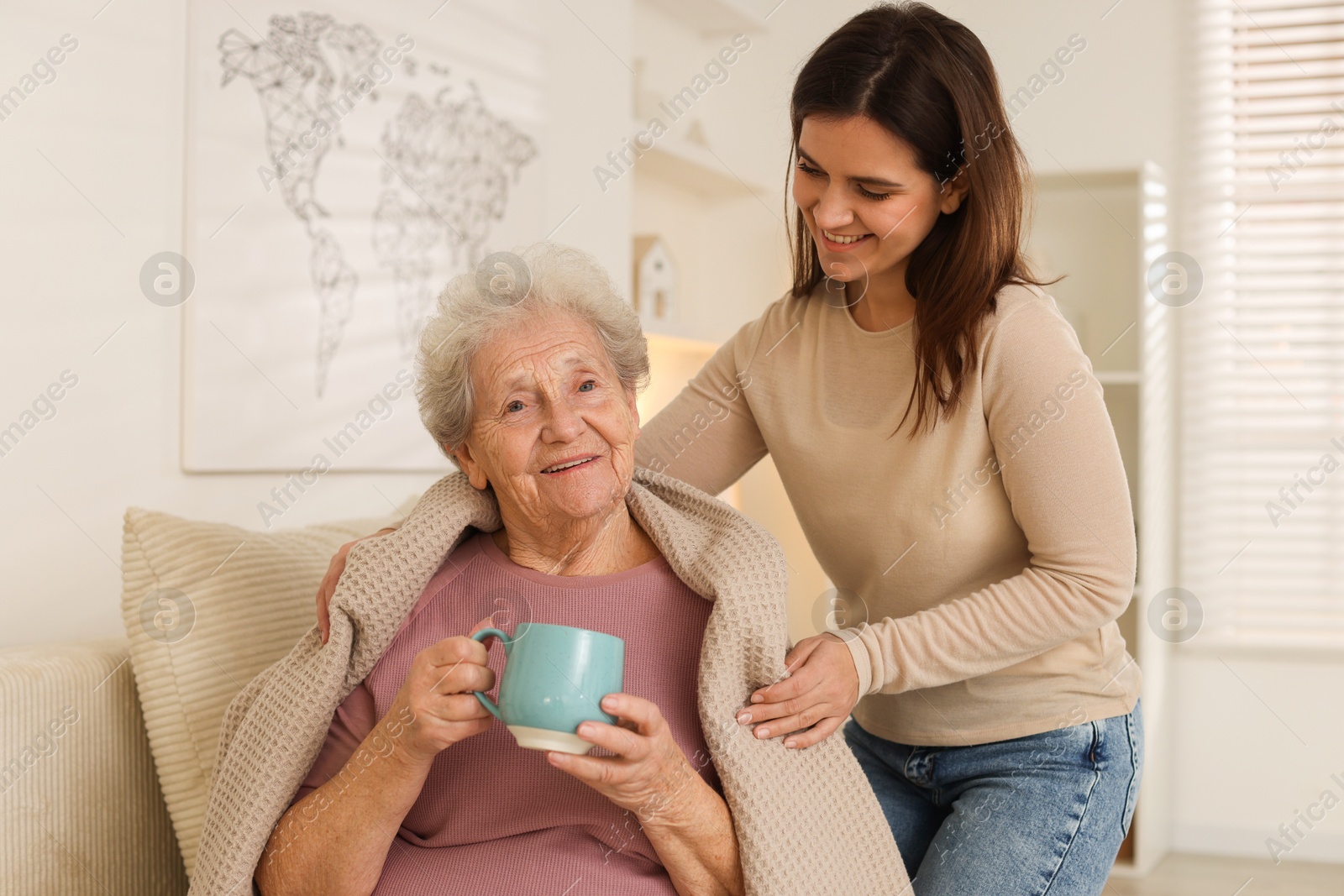 Photo of Granddaughter giving hot drink to her grandmother at home. Elderly care