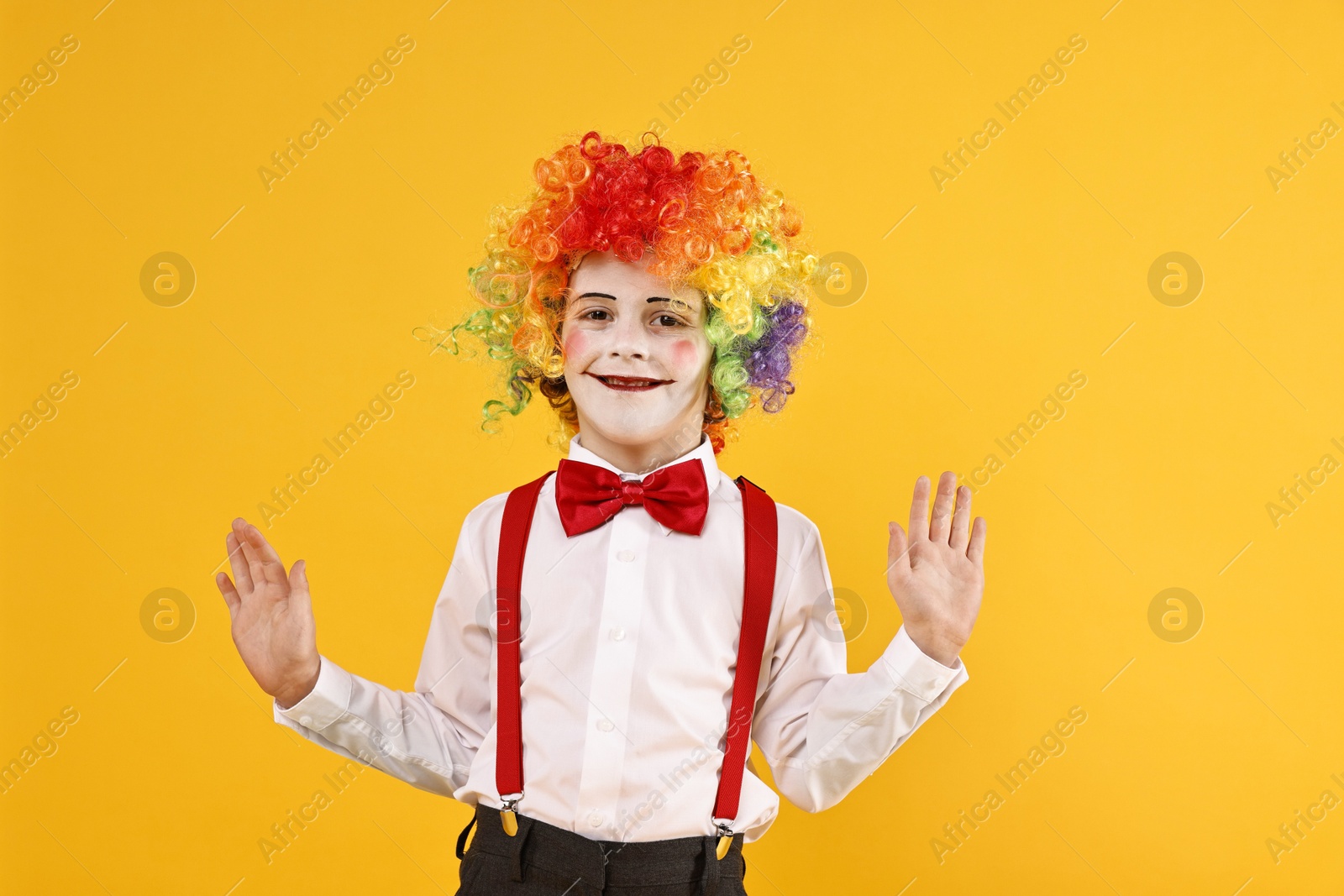 Photo of Happy little boy dressed like clown on yellow background. Surprise party