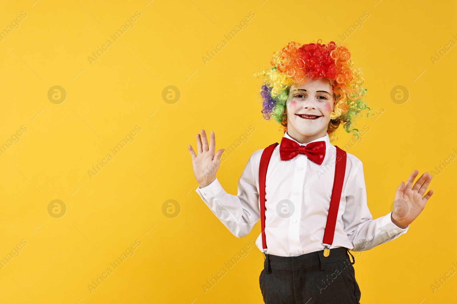 Photo of Happy little boy dressed like clown on yellow background, space for text. Surprise party