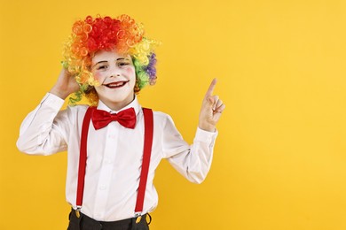 Photo of Happy little boy dressed like clown pointing at something on yellow background, space for text. Surprise party