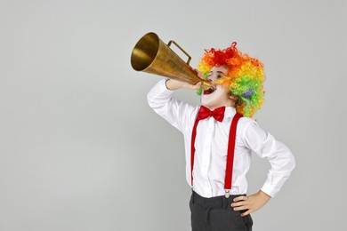 Photo of Little boy dressed like clown shouting in megaphone on grey background, space for text. Surprise party