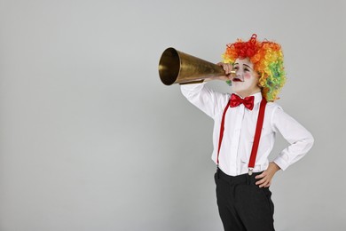 Photo of Little boy dressed like clown with megaphone on grey background, space for text. Surprise party