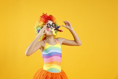 Photo of Girl dressed like clown with blowers on yellow background. Surprise party