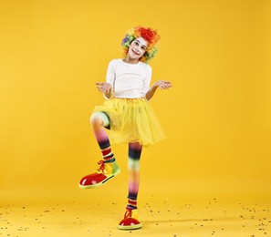 Photo of Cute girl dressed like clown having fun and confetti on yellow background. Surprise party