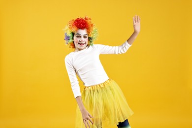 Photo of Happy girl dressed like clown on yellow background. Surprise party