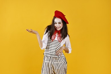 Happy girl dressed like mime holding something on yellow background. Surprise party