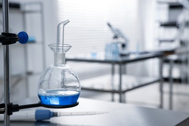 Photo of Flask with blue liquid on retort stand in laboratory, closeup. Space for text