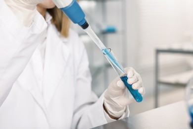 Scientist with micropipette and test tube working in laboratory, closeup