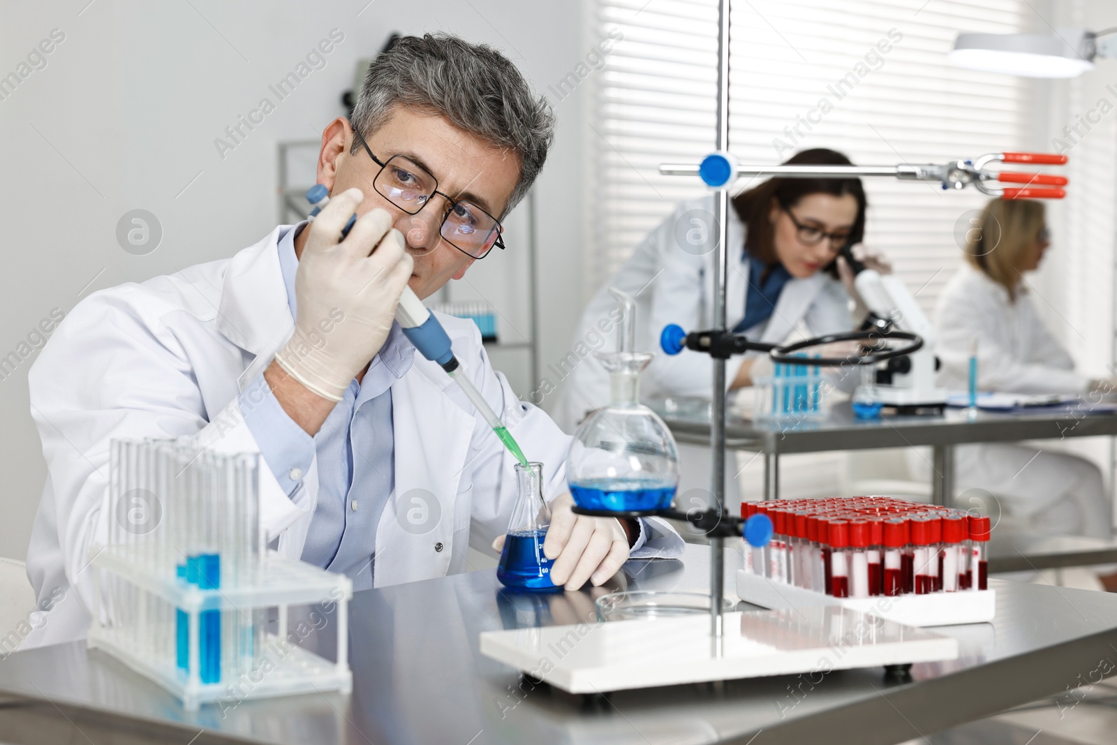 Photo of Scientist with micropipette and flask working in laboratory