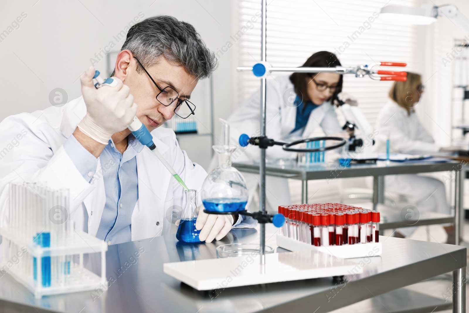 Photo of Scientist with micropipette and flask working in laboratory