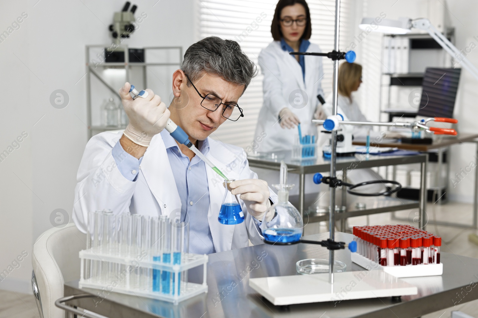 Photo of Scientist with micropipette and flask working in laboratory