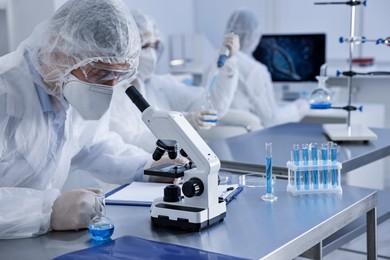 Photo of Scientist in protective suit working with microscope at laboratory