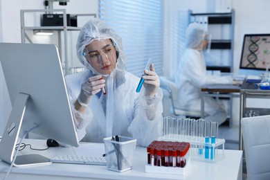 Scientist working with computer and chemical glassware at table in laboratory