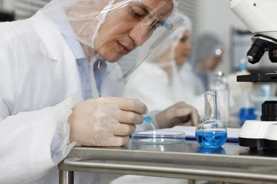 Photo of Scientist dripping sample into Petri dish at table in laboratory, closeup