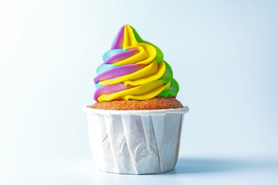 Photo of Tasty cupcake with colorful cream on light blue background, closeup