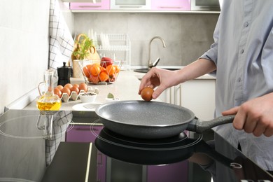 Photo of Woman breaking egg into frying pan in kitchen, closeup