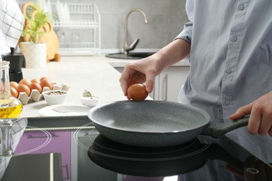 Photo of Woman breaking egg into frying pan in kitchen, closeup