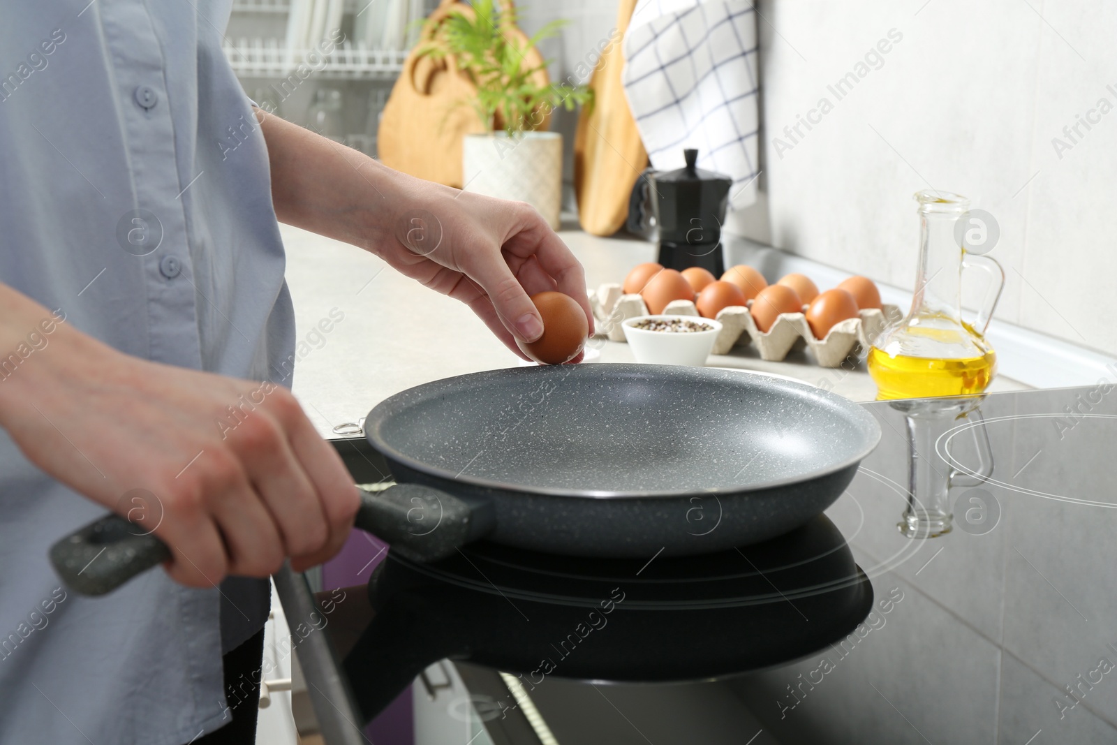 Photo of Woman breaking egg into frying pan in kitchen, closeup