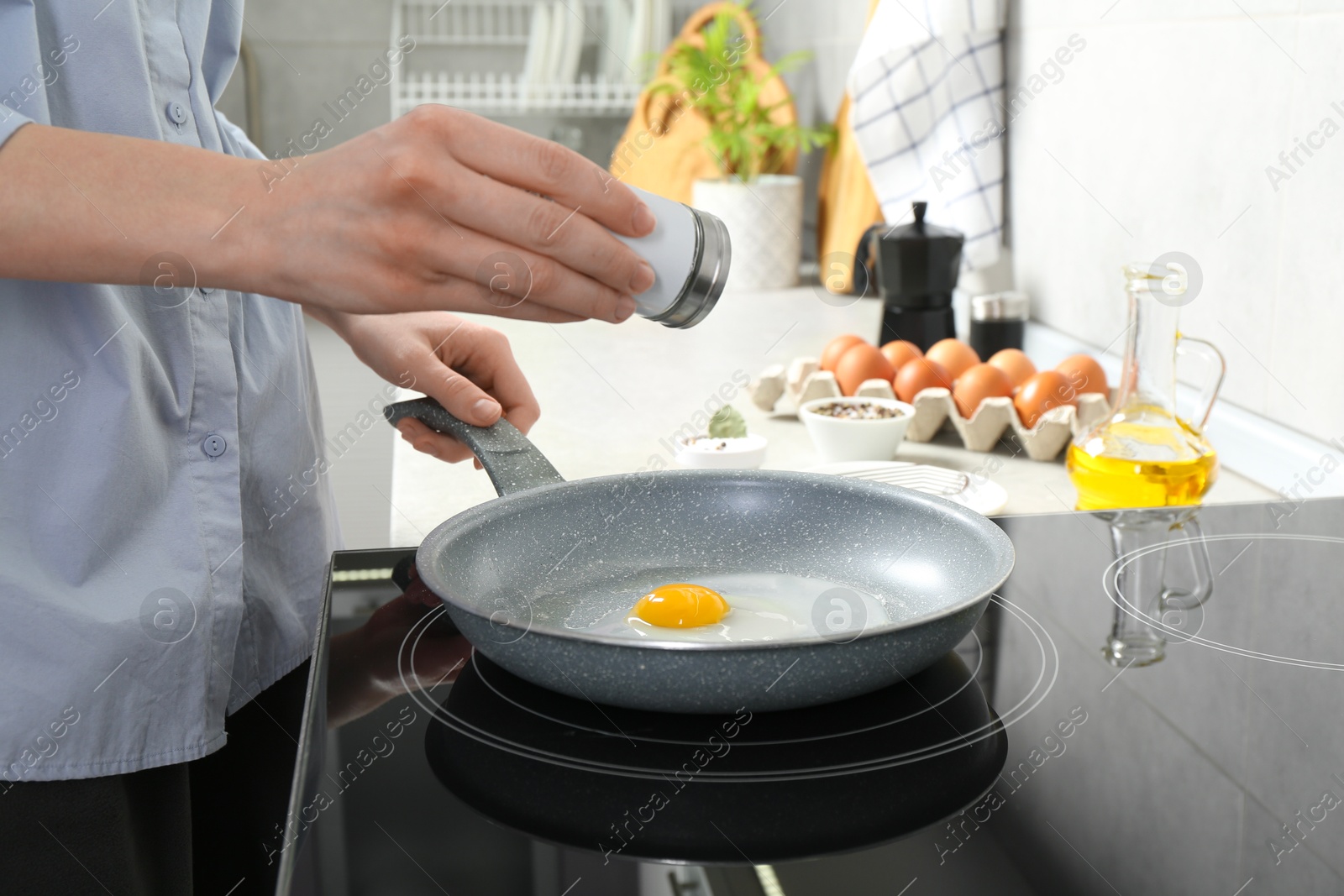 Photo of Woman adding salt into frying pan while cooking eggs on cooktop in kitchen, closeup