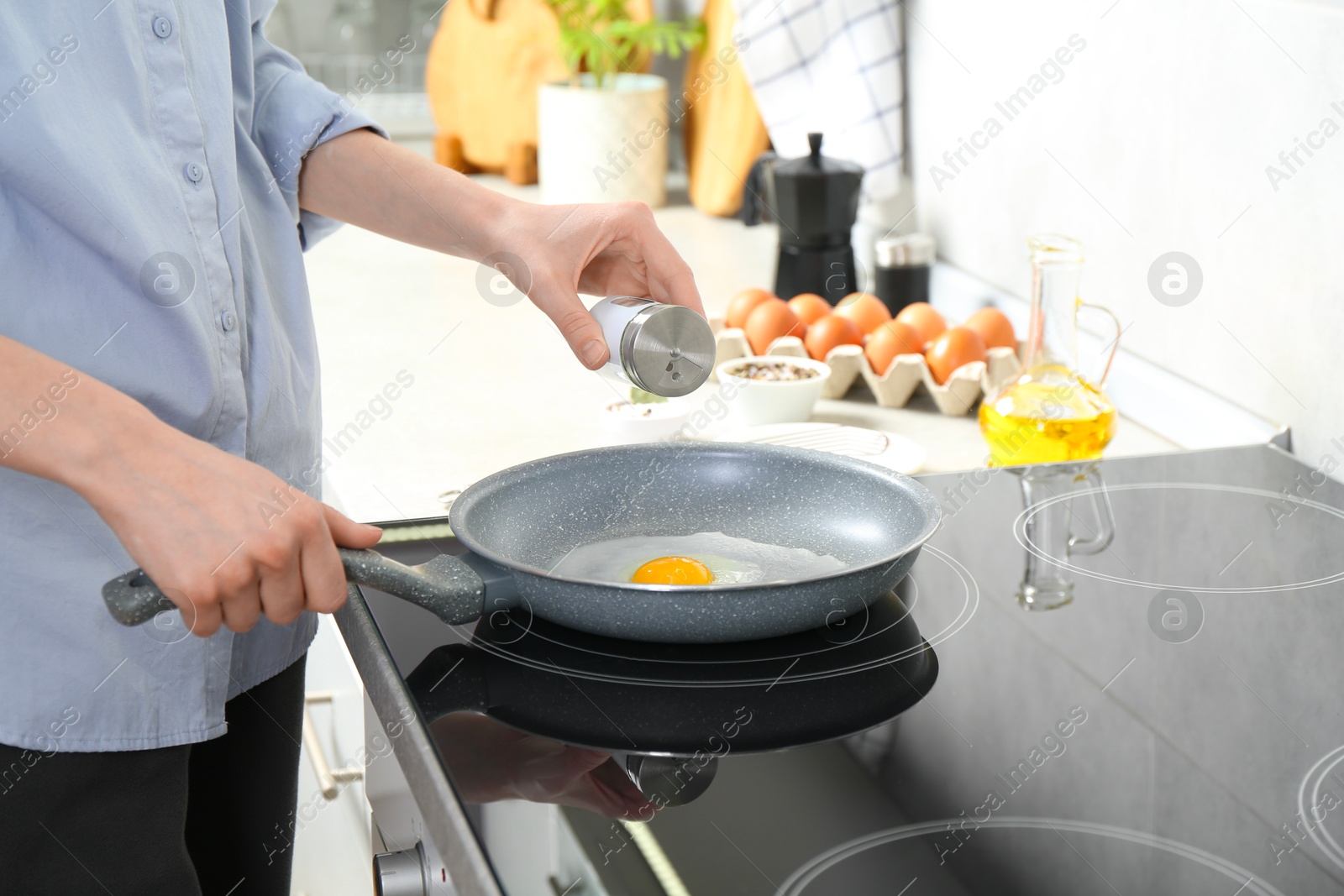 Photo of Woman adding salt into frying pan while cooking eggs on cooktop in kitchen, closeup