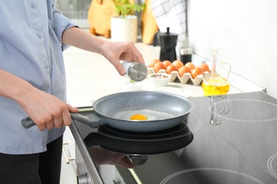 Woman adding salt into frying pan while cooking eggs on cooktop in kitchen, closeup