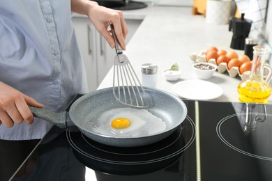 Photo of Man cooking egg in frying pan on cooktop indoors, closeup