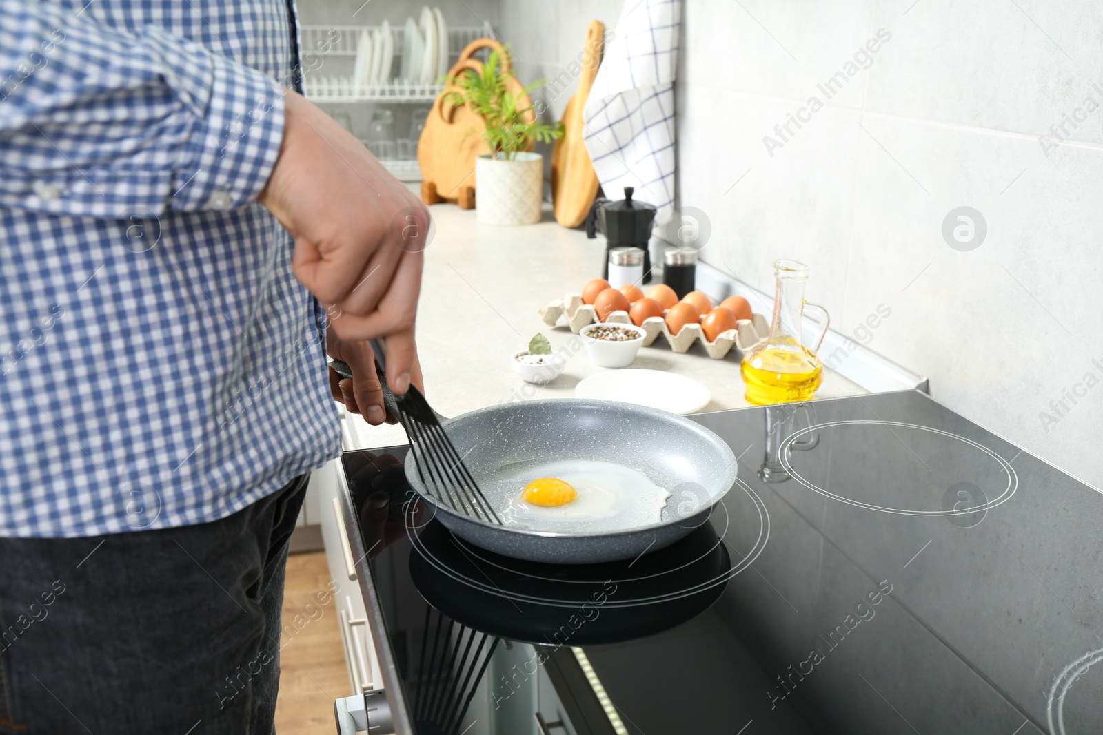 Photo of Man cooking egg in frying pan on cooktop indoors, closeup