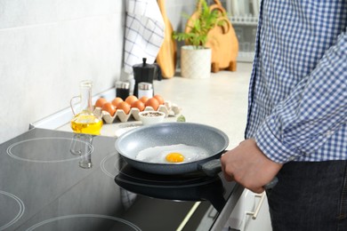 Photo of Man cooking egg in frying pan on cooktop indoors, closeup