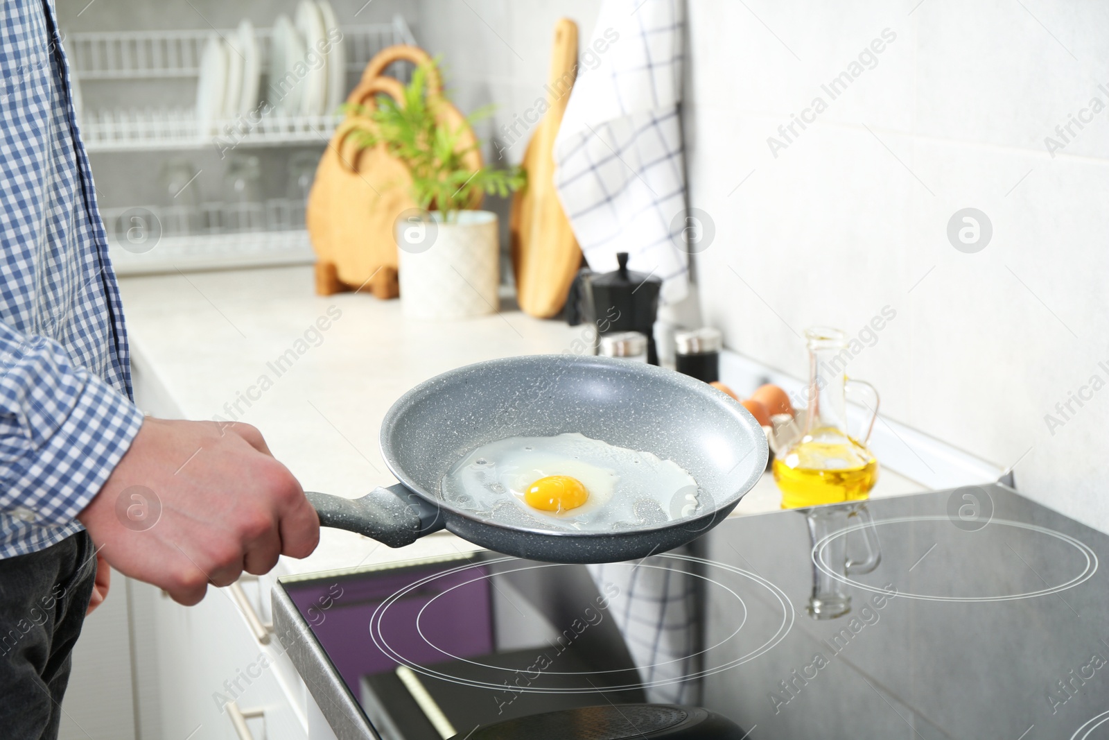 Photo of Man cooking egg in frying pan on cooktop indoors, closeup