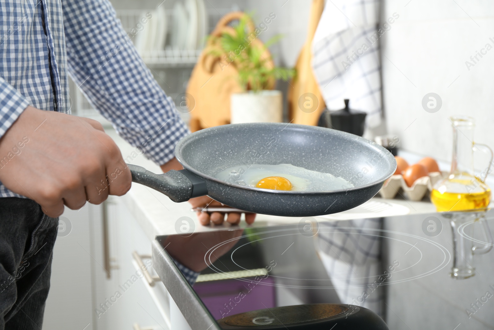 Photo of Man cooking egg in frying pan on cooktop indoors, closeup