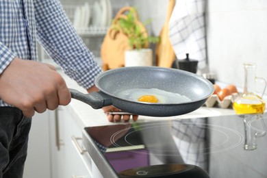 Man cooking egg in frying pan on cooktop indoors, closeup