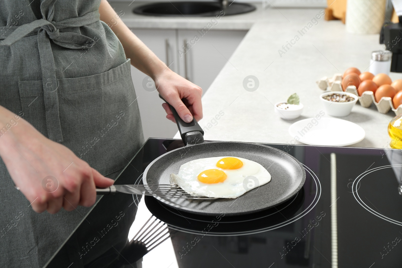 Photo of Woman taking fried eggs from frying pan in kitchen, closeup