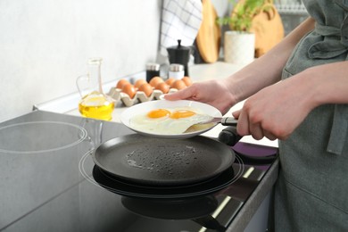 Photo of Woman putting tasty fried eggs onto plate in kitchen, closeup