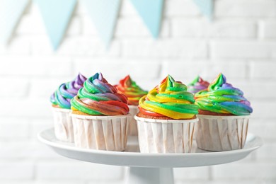 Photo of Delicious cupcakes with colorful cream on stand near white brick wall, closeup