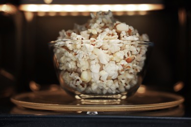 Photo of Bowl of tasty popcorn in microwave oven, closeup