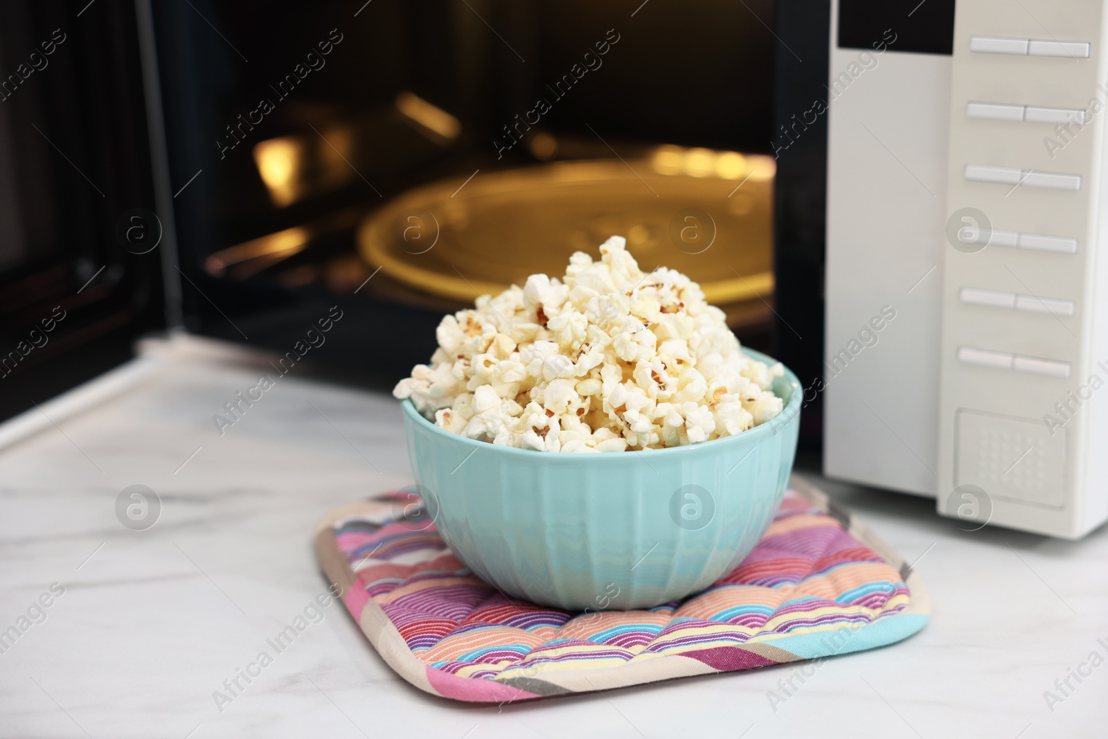 Photo of Tasty popcorn in bowl near microwave oven on light marble table, closeup