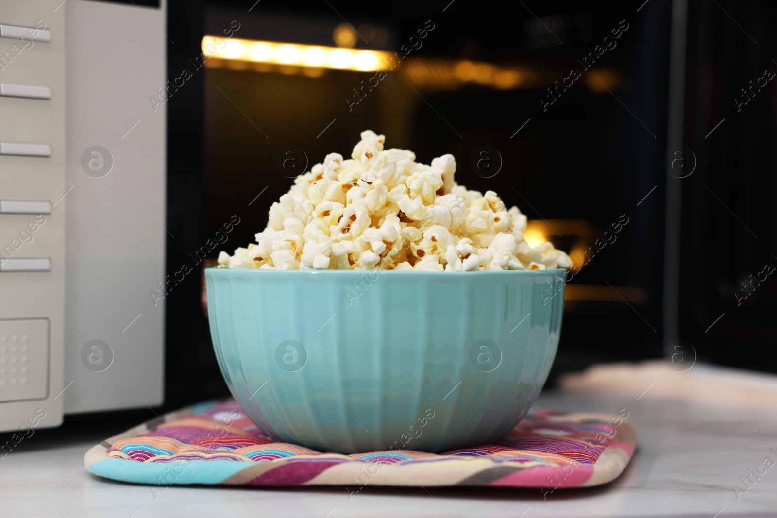 Photo of Tasty popcorn in bowl near microwave oven on light table, closeup