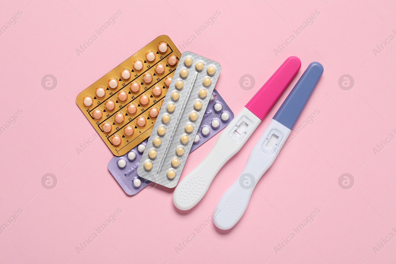 Photo of Blisters of oral contraceptive pills and pregnancy tests on pink background, flat lay