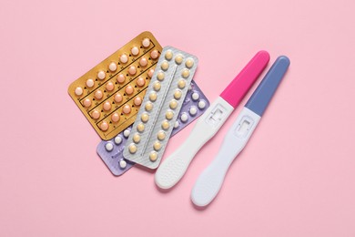 Photo of Blisters of oral contraceptive pills and pregnancy tests on pink background, flat lay