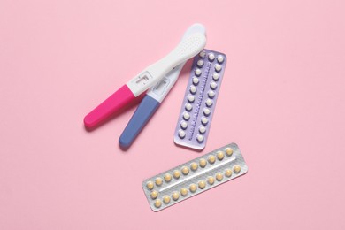 Blisters of oral contraceptive pills and pregnancy test on pink background, flat lay