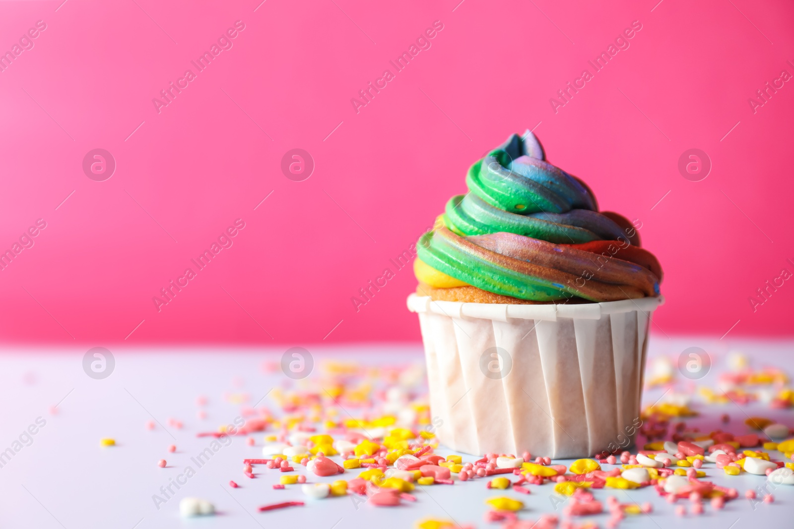 Photo of Delicious cupcake with colorful cream and confetti on light table, closeup. Space for text