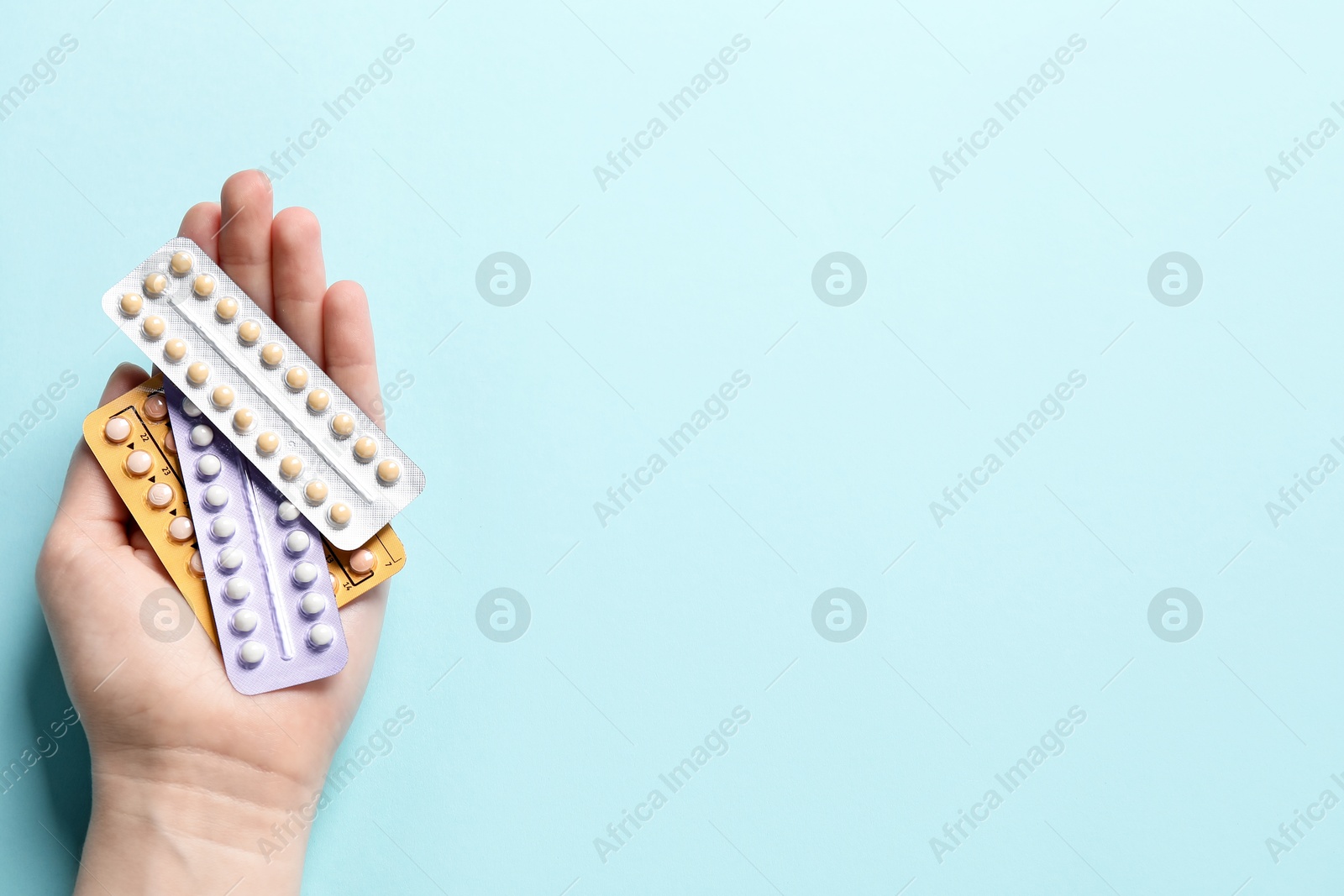 Photo of Woman holding blisters of contraceptive pills on light blue background, closeup. Space for text