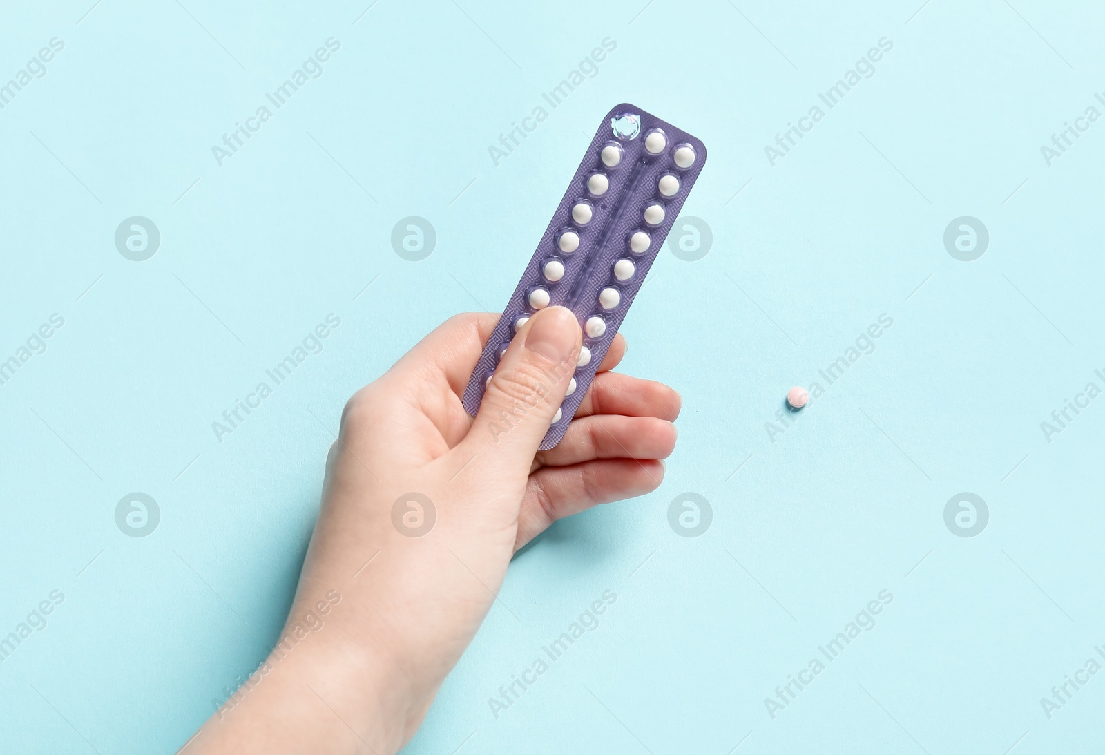 Photo of Woman holding blister of contraceptive pills on light blue background, closeup