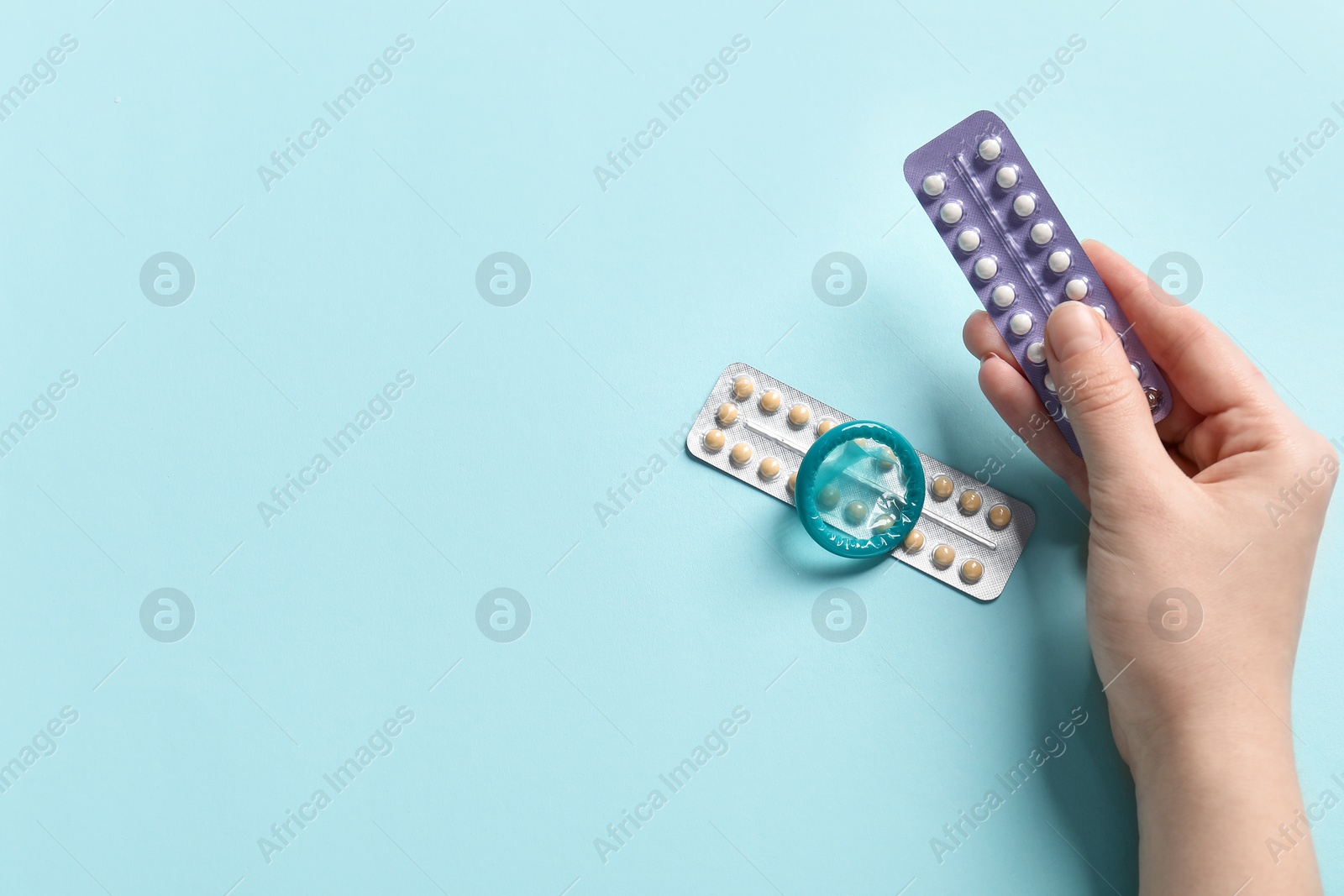 Photo of Woman with blisters of contraceptive pills and condom on light blue background, closeup. Space for text