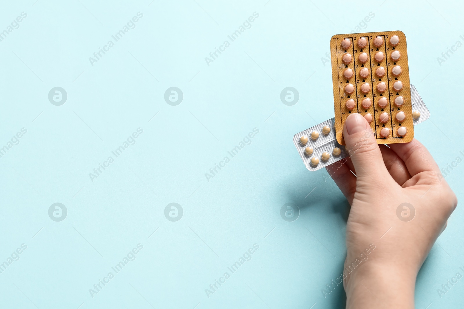 Photo of Woman holding blisters of contraceptive pills on light blue background, closeup. Space for text