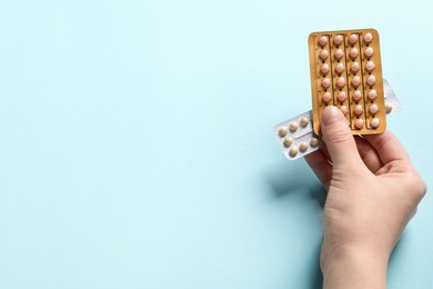 Photo of Woman holding blisters of contraceptive pills on light blue background, closeup. Space for text