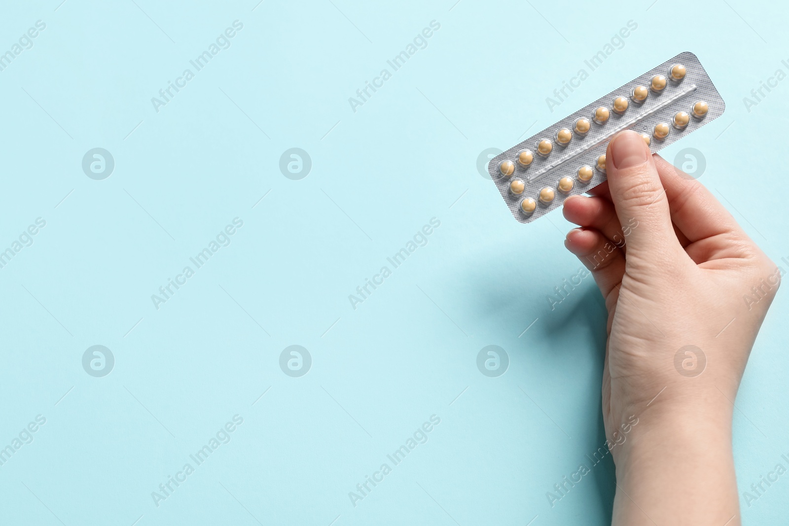 Photo of Woman holding blister of contraceptive pills on light blue background, closeup. Space for text