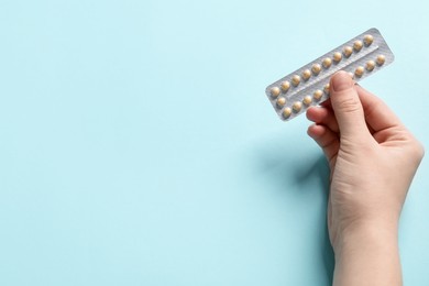 Photo of Woman holding blister of contraceptive pills on light blue background, closeup. Space for text